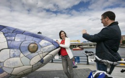 Two visitors taking photo at The Big Fish sculpture beside the River Lagan